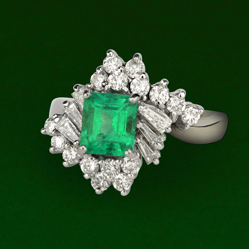 Platinum cocktail ring featuring a square-cut green emerald surrounded by round brilliant and baguette diamonds