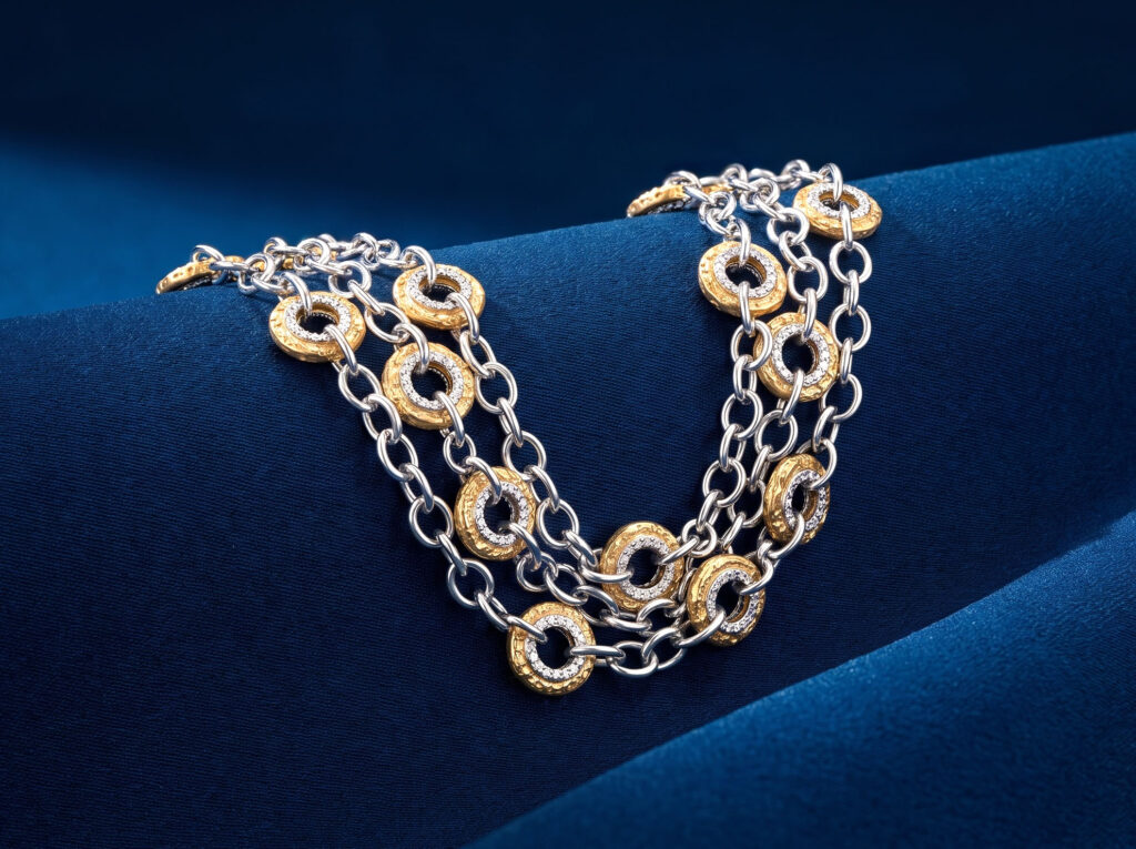 White gold link chain bracelet interwoven with diamond-accented textured yellow gold circular stations on blue silk